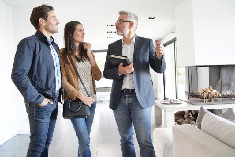 A couple and an agent discuss paperwork across a dining table in a well-lit, lived-in family home.